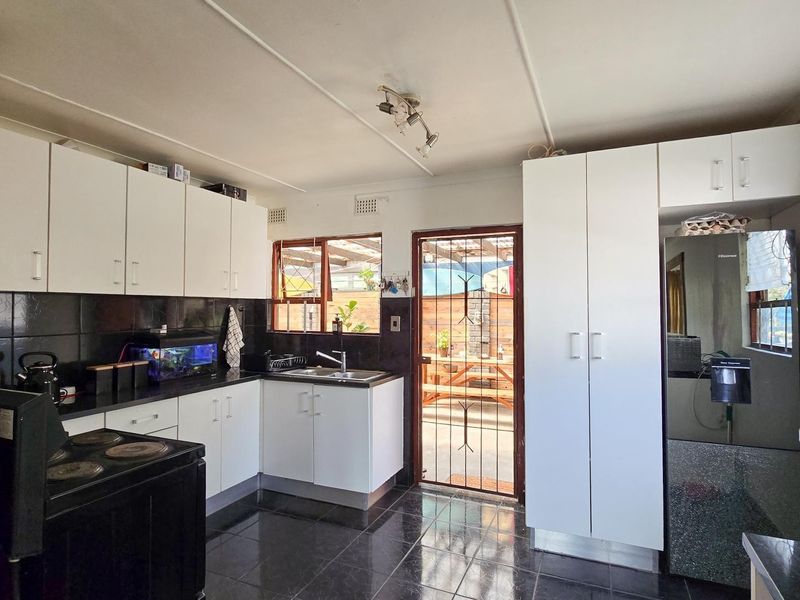 Functional kitchen featuring white cabinetry, black tiled splashbacks, dark floor tiles, and direct access to an outdoor patio area.