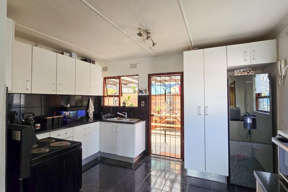 Functional kitchen featuring white cabinetry, black tiled splashbacks, dark floor tiles, and direct access to an outdoor patio area.
