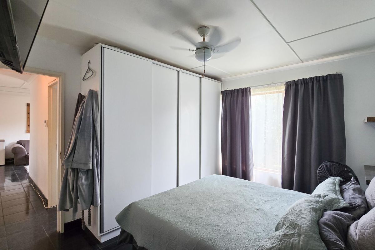 A bedroom featuring a large built-in wardrobe, ceiling fan, and tiled flooring, offering a functional and neutral living space.