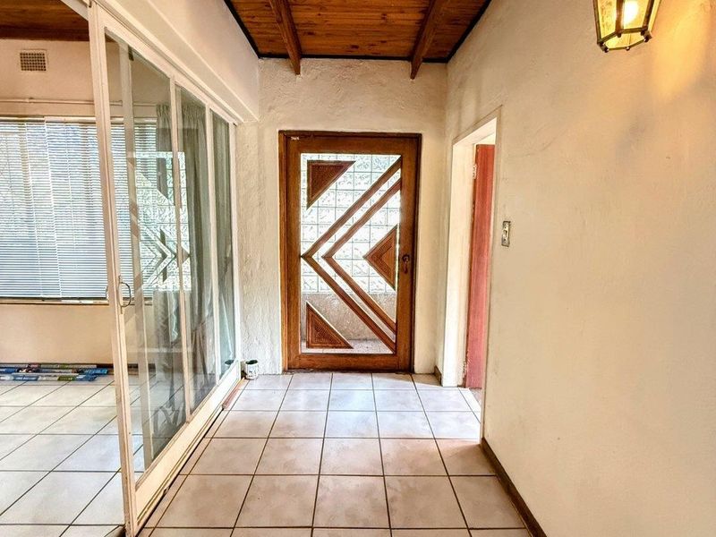 Entrance hall featuring a timber-clad ceiling, ceramic tiled flooring, and a decorative glass-panelled front door leading into the home.