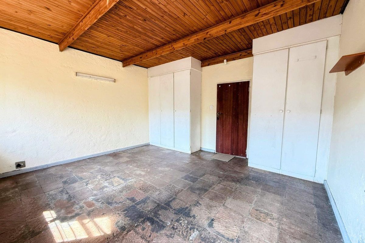 An empty bedroom featuring exposed timber beam ceilings, built-in cupboards, and tiled flooring, offering a blank canvas for renovation.