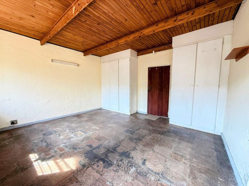 An empty bedroom featuring exposed timber beam ceilings, built-in cupboards, and tiled flooring, offering a blank canvas for renovation.