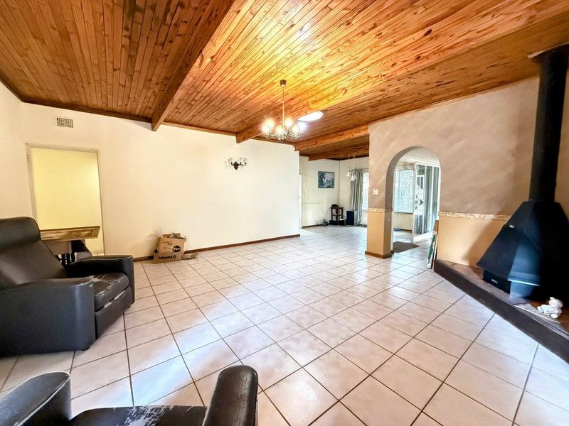Spacious living area featuring a timber-clad vaulted ceiling, ceramic floor tiles, and a prominent freestanding fireplace, offering a versatile layout for comfortable family living.