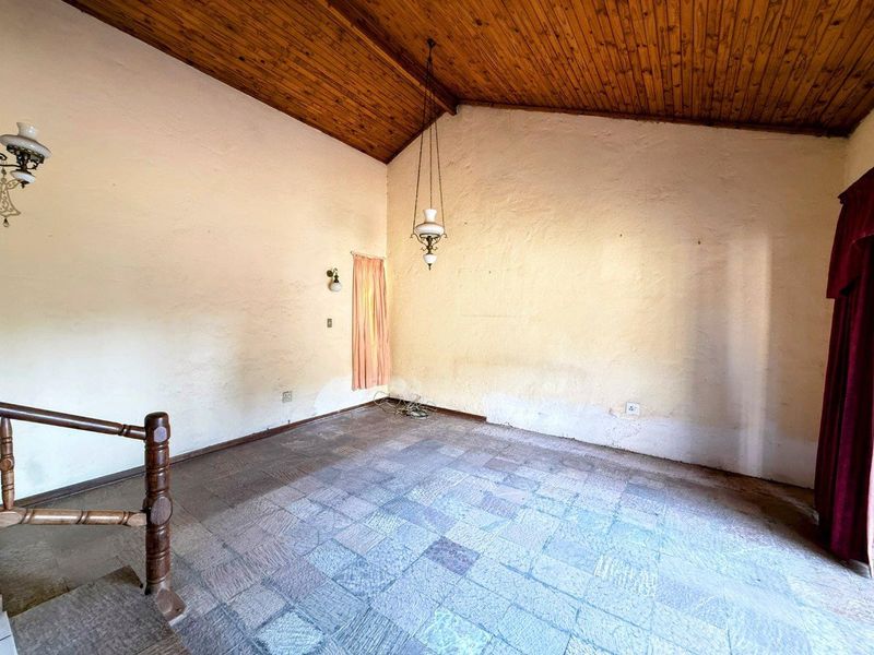 An empty living room featuring a high timber raked ceiling, stone tile flooring, and a timber balustrade, offering a blank canvas for renovation.
