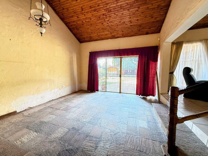 Spacious living area featuring a vaulted timber-clad ceiling, stone tile flooring, and direct access to the garden through a sliding glass door.