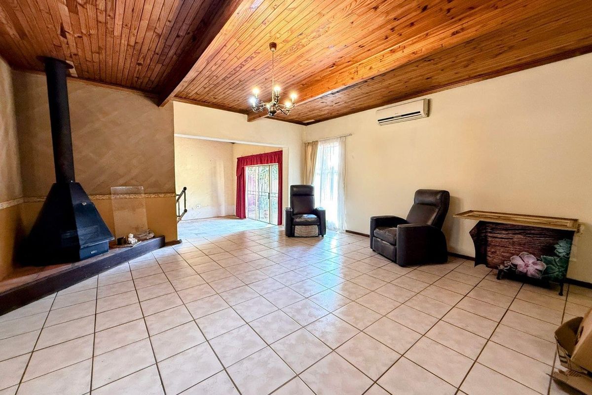 Spacious living area featuring a vaulted timber ceiling, tiled flooring, and a prominent freestanding fireplace, offering a versatile space for relaxation.