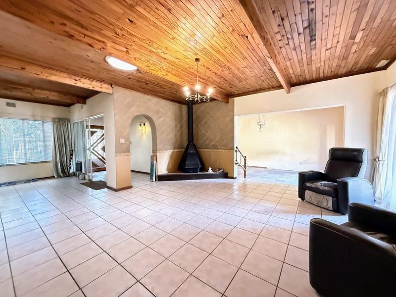 Spacious living area featuring a high exposed timber ceiling, a central freestanding fireplace, and tiled flooring with an open-plan layout.