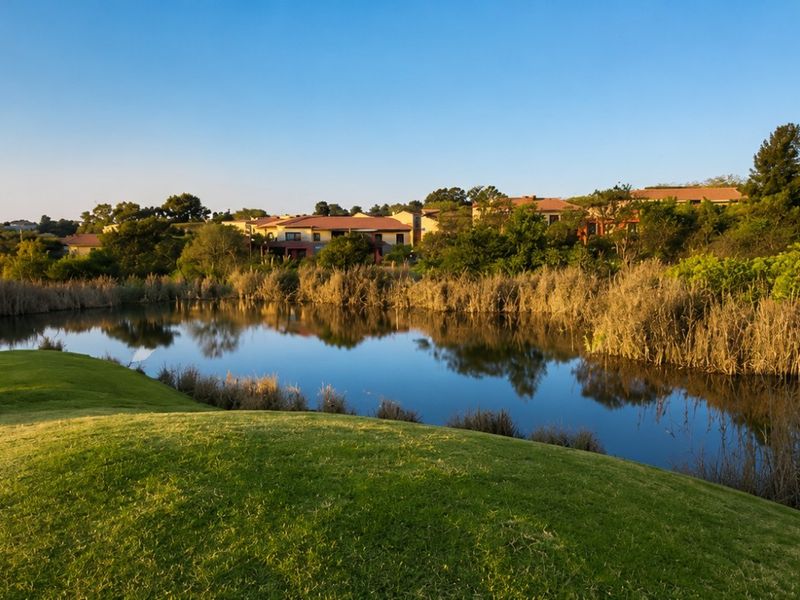 A scenic view overlooking a tranquil pond and manicured golf course fairway with residential buildings in the background.