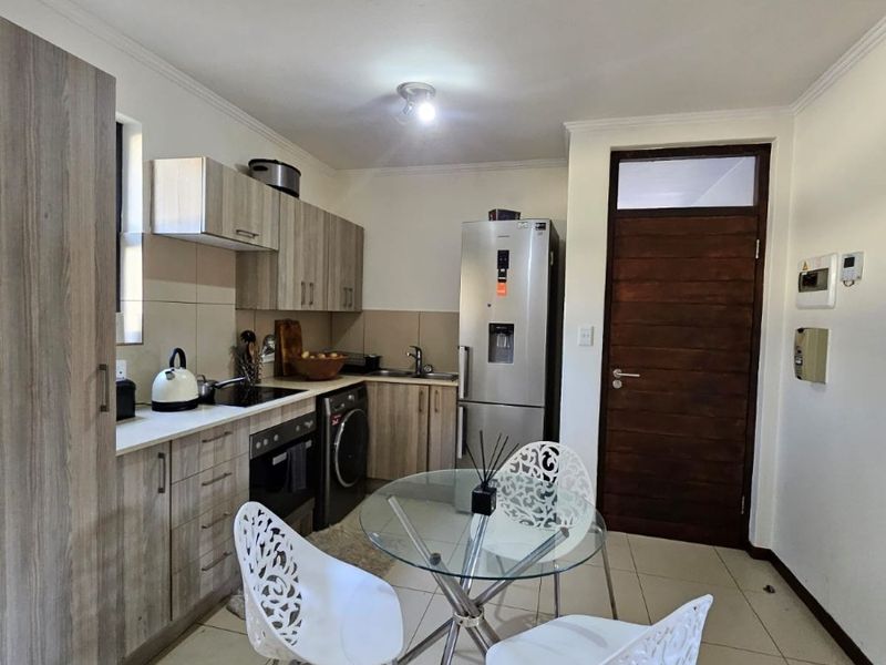 Compact open-plan kitchen and dining area featuring modern wood-finish cabinetry, tiled flooring, and integrated appliances, providing a functional and efficient living space.