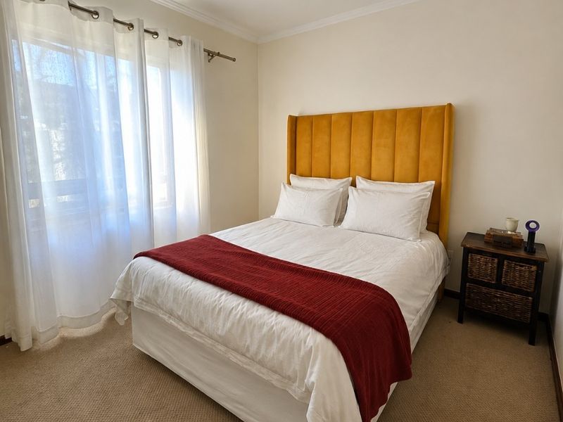 A well-maintained bedroom featuring neutral walls, carpeted flooring, and a ceiling-mounted spotlight fixture, offering a comfortable and functional living space.