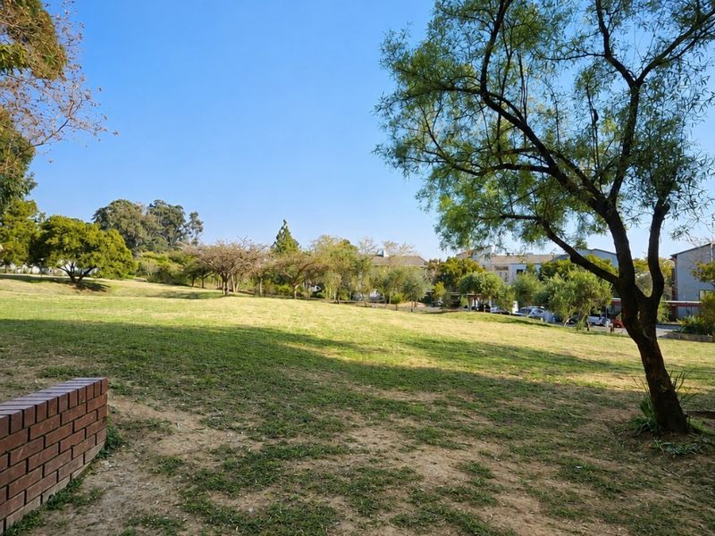 A spacious open garden area featuring a brick retaining wall and mature trees, providing a pleasant outdoor green space.