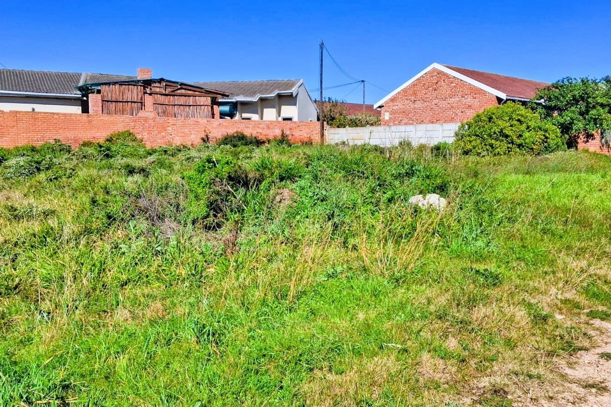 A vacant residential plot featuring overgrown grass and established brick and precast concrete boundary walls, offering a clear space for future development.