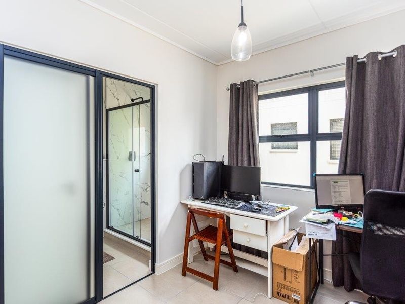 A bedroom featuring tiled flooring, an en-suite bathroom with a glass shower enclosure, and a window with dark curtains.