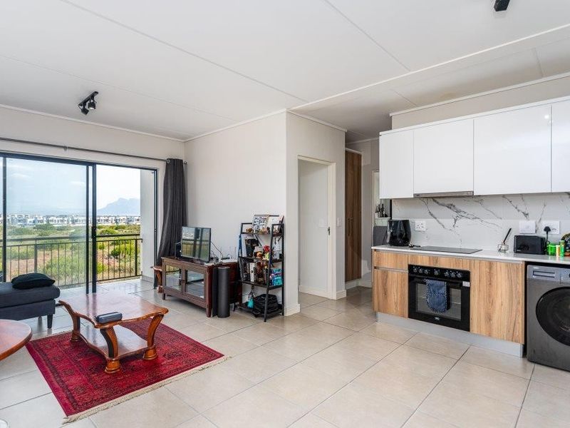 Modern open-plan living area featuring a sleek kitchen with built-in appliances, marble-look splashback, and large sliding doors leading to a balcony with scenic views.