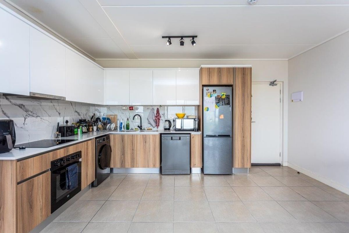 Modern kitchen featuring sleek white and wood-grain cabinetry, marble-look splashback, integrated oven, hob, and tiled flooring in an open-plan layout.