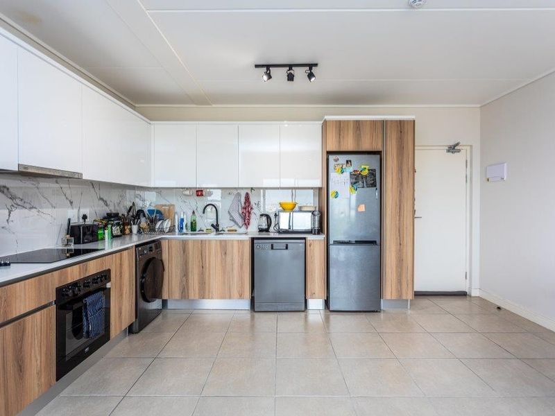 Modern kitchen featuring sleek white and wood-grain cabinetry, marble-look splashback, integrated oven, hob, and tiled flooring in an open-plan layout.