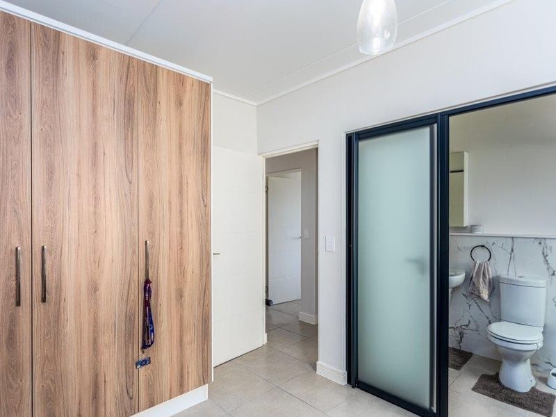 A well-maintained bedroom featuring wood-finish built-in wardrobes, tiled flooring, and a modern en-suite bathroom with a frosted glass door.