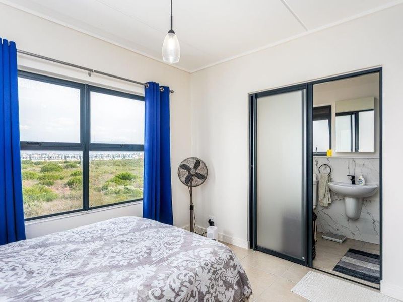 A bright bedroom featuring tiled flooring, large windows with natural light, and an integrated en-suite bathroom with modern finishes.