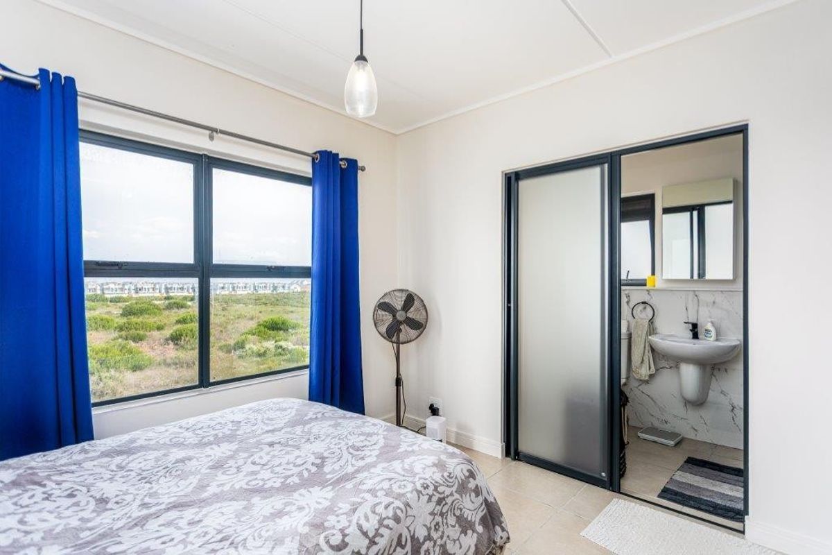 A bright bedroom featuring tiled flooring, large windows with natural light, and an integrated en-suite bathroom with modern finishes.