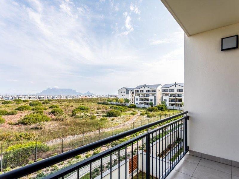 A clean, modern balcony featuring tiled flooring and a metal balustrade, offering expansive views of the surrounding landscape and distant mountains.
