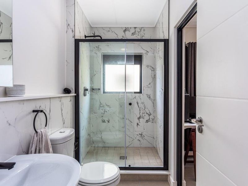 Modern bathroom featuring marble-look wall tiles, a walk-in shower with black frame sliding doors, and contemporary black fixtures.