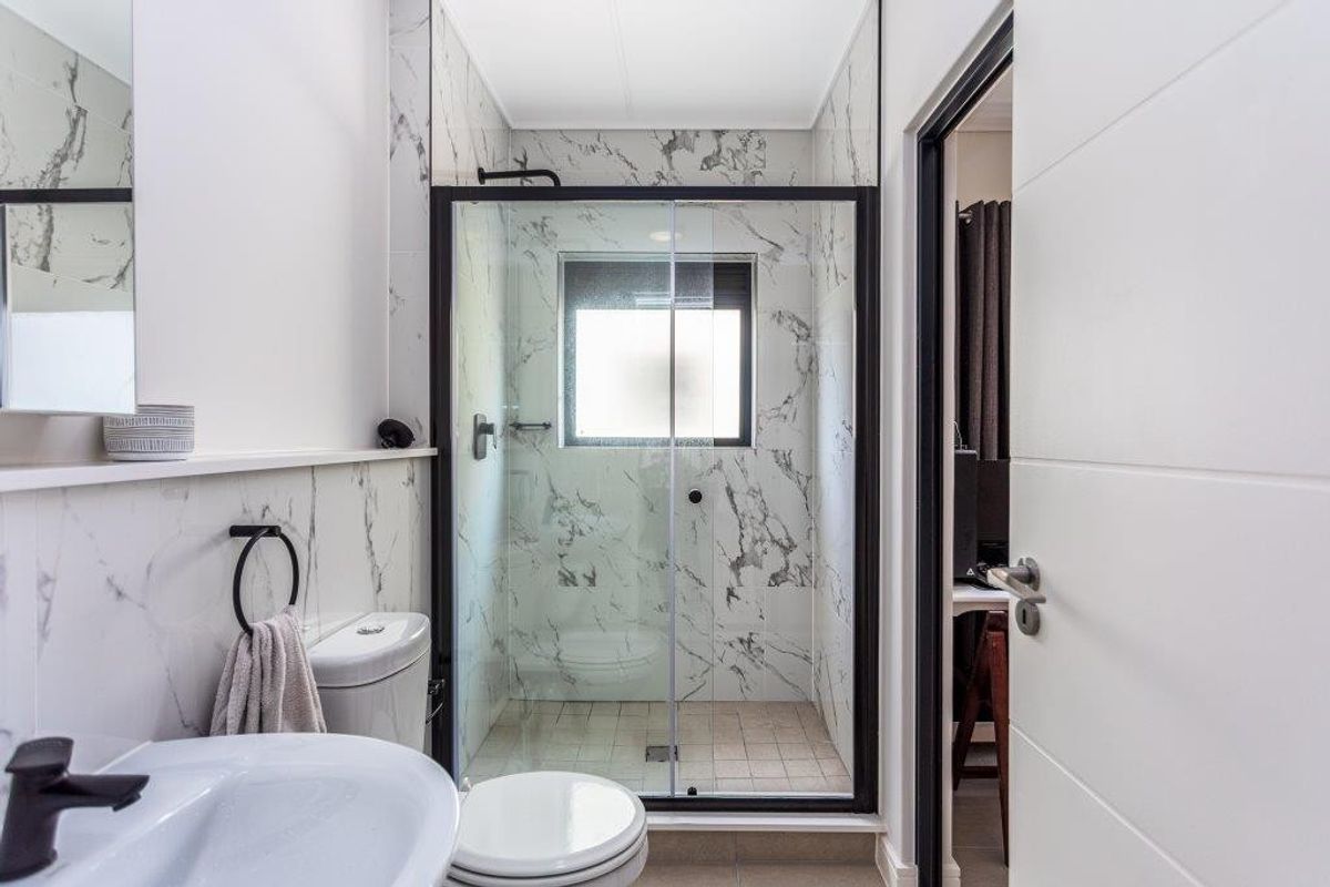 Modern bathroom featuring marble-look wall tiles, a walk-in shower with black frame sliding doors, and contemporary black fixtures.
