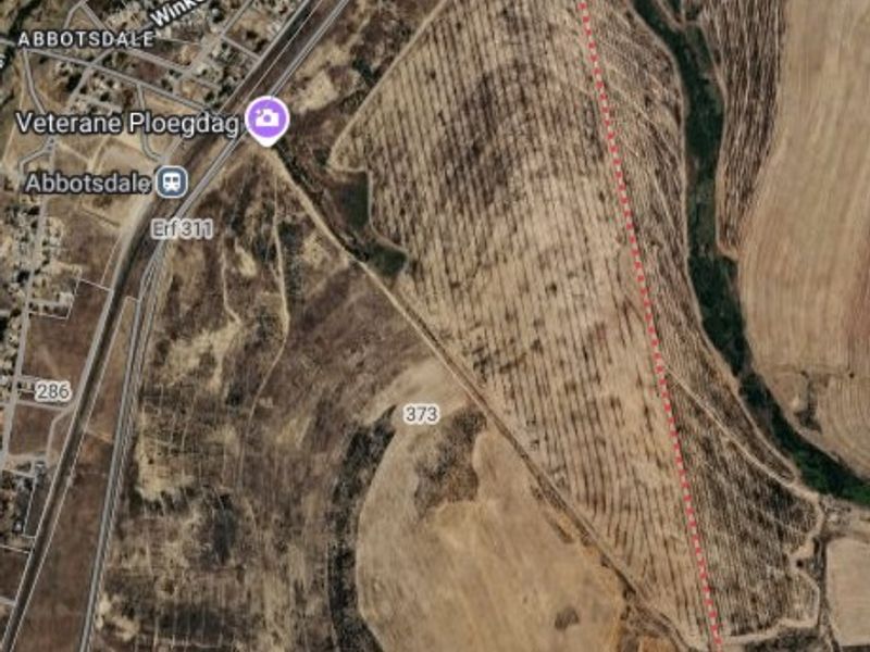 An aerial view of a large vacant agricultural land plot with marked boundaries, situated near local infrastructure and roads.