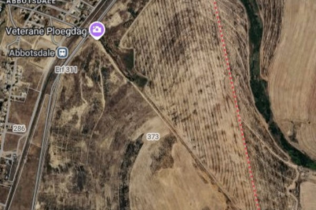 An aerial view of a large vacant agricultural land plot with marked boundaries, situated near local infrastructure and roads.