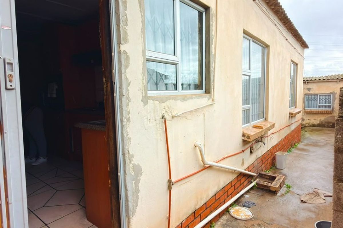 Rear exterior view of the property showing tiled roof, aluminium windows, and visible wear to the exterior wall plaster and paint finishes.