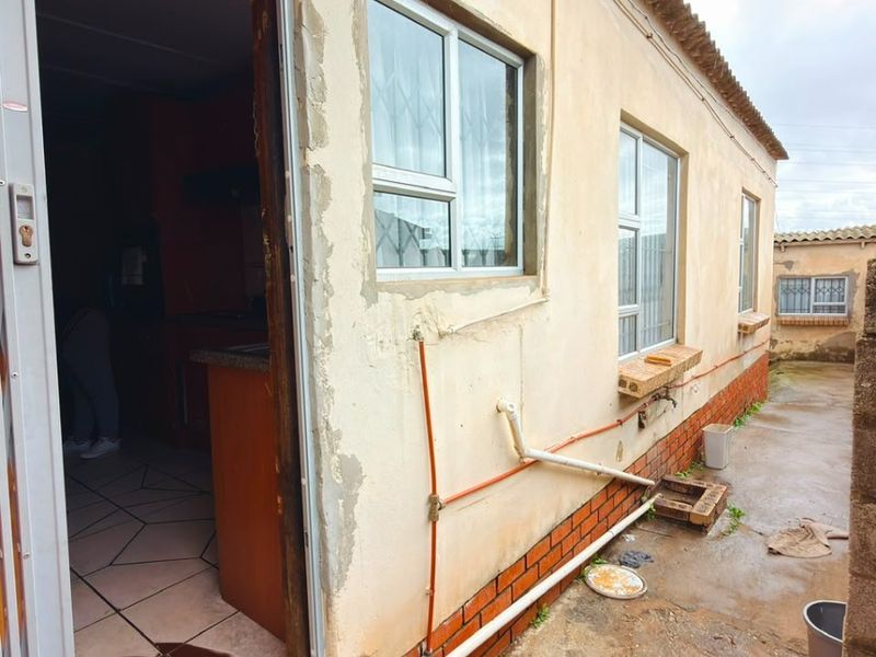 Rear exterior view of the property showing tiled roof, aluminium windows, and visible wear to the exterior wall plaster and paint finishes.