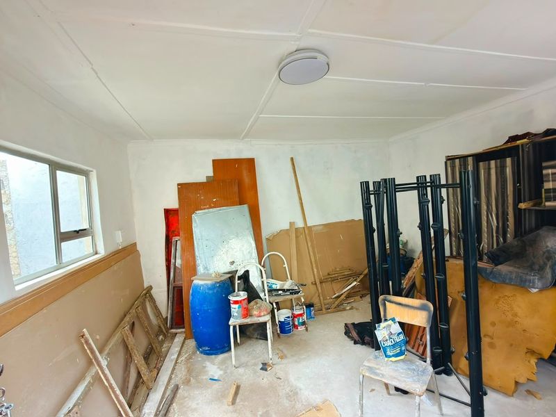 An unfinished utility space featuring concrete flooring and an aluminium window, currently used for storage and requiring cosmetic completion.