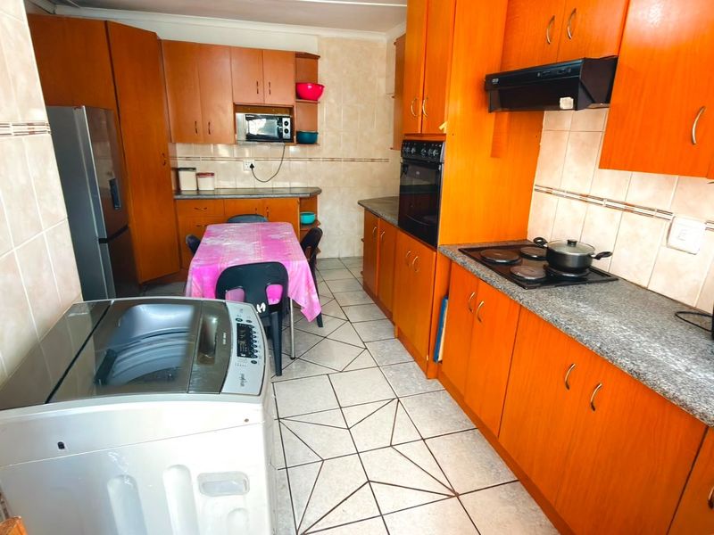 A functional kitchen featuring wood-tone cabinetry, granite-look laminate countertops, built-in oven, electric hob, and tiled flooring throughout.