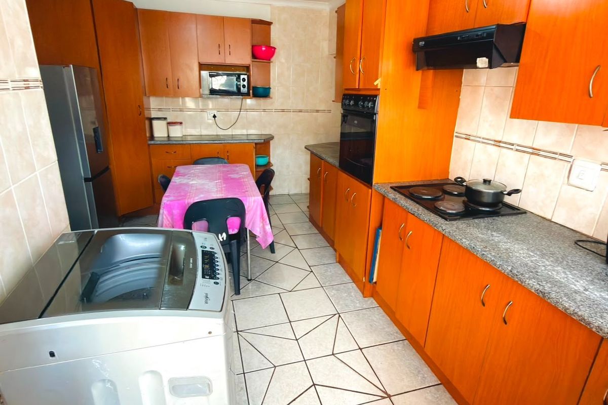A functional kitchen featuring wood-tone cabinetry, granite-look laminate countertops, built-in oven, electric hob, and tiled flooring throughout.
