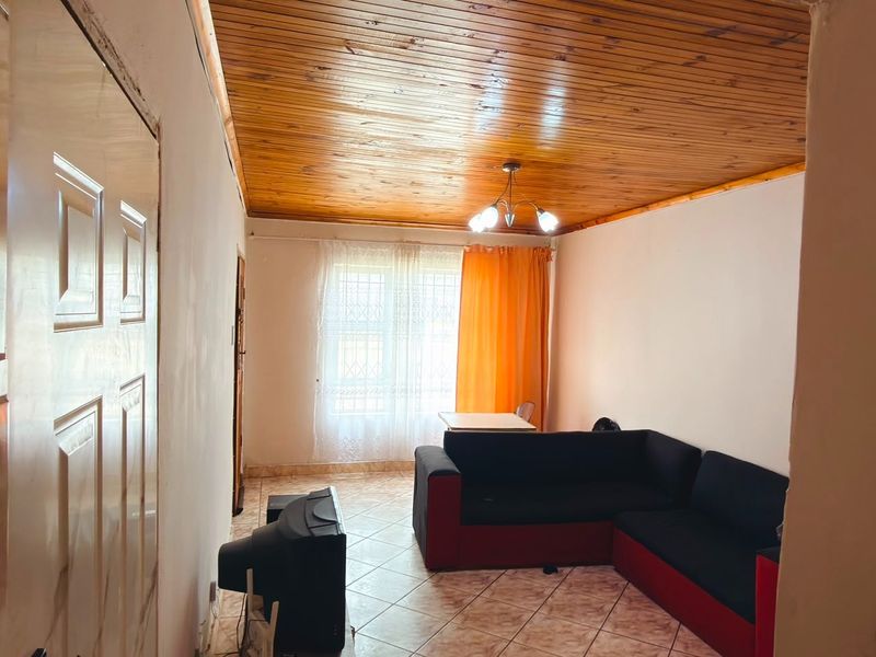 Living room featuring a timber tongue and groove ceiling, ceramic tiled flooring, and a window fitted with security bars.
