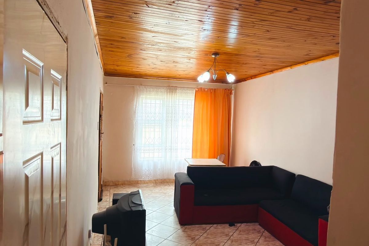 Living room featuring a timber tongue and groove ceiling, ceramic tiled flooring, and a window fitted with security bars.