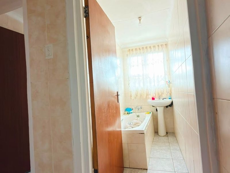 A compact bathroom featuring a pedestal basin, built-in bathtub, and full-height ceramic wall tiling, requiring cosmetic updates to modernize the space.