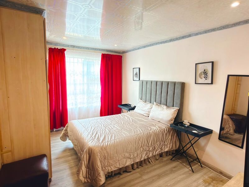 A bedroom featuring laminate flooring and decorative ceiling tiles, equipped with security bars on the window.