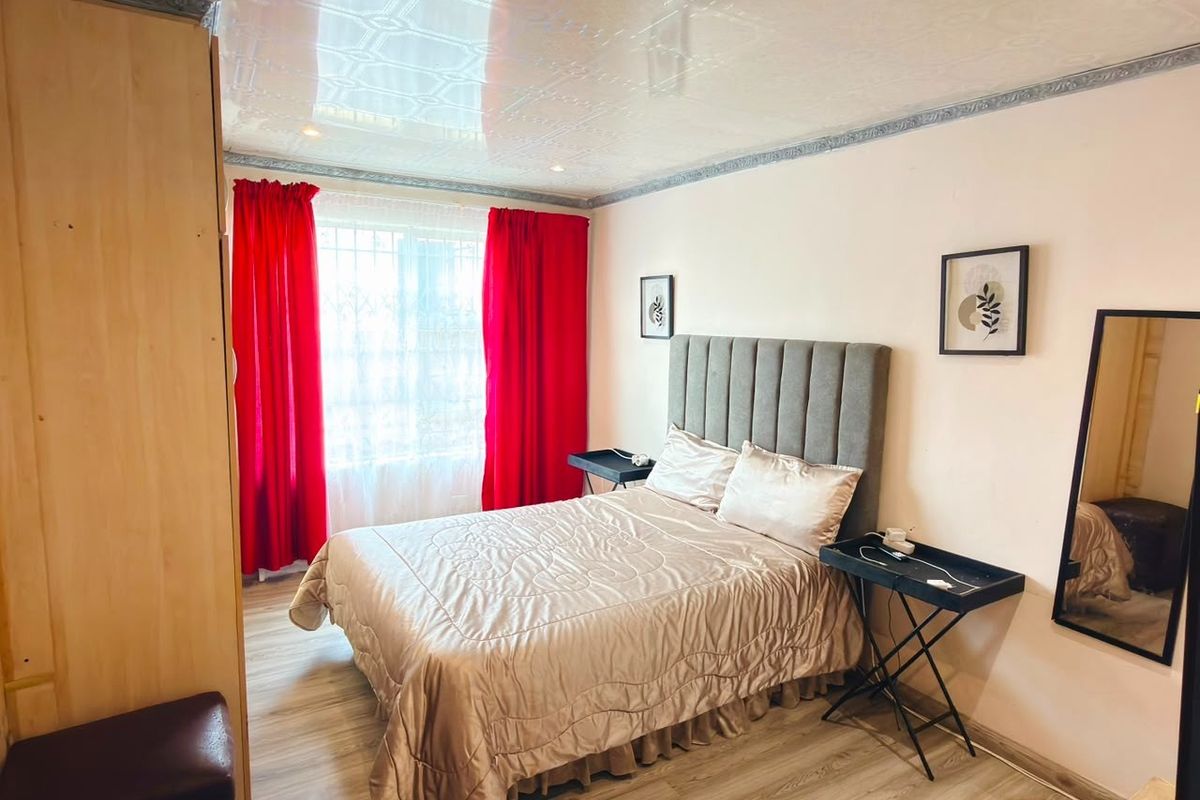 A bedroom featuring laminate flooring and decorative ceiling tiles, equipped with security bars on the window.