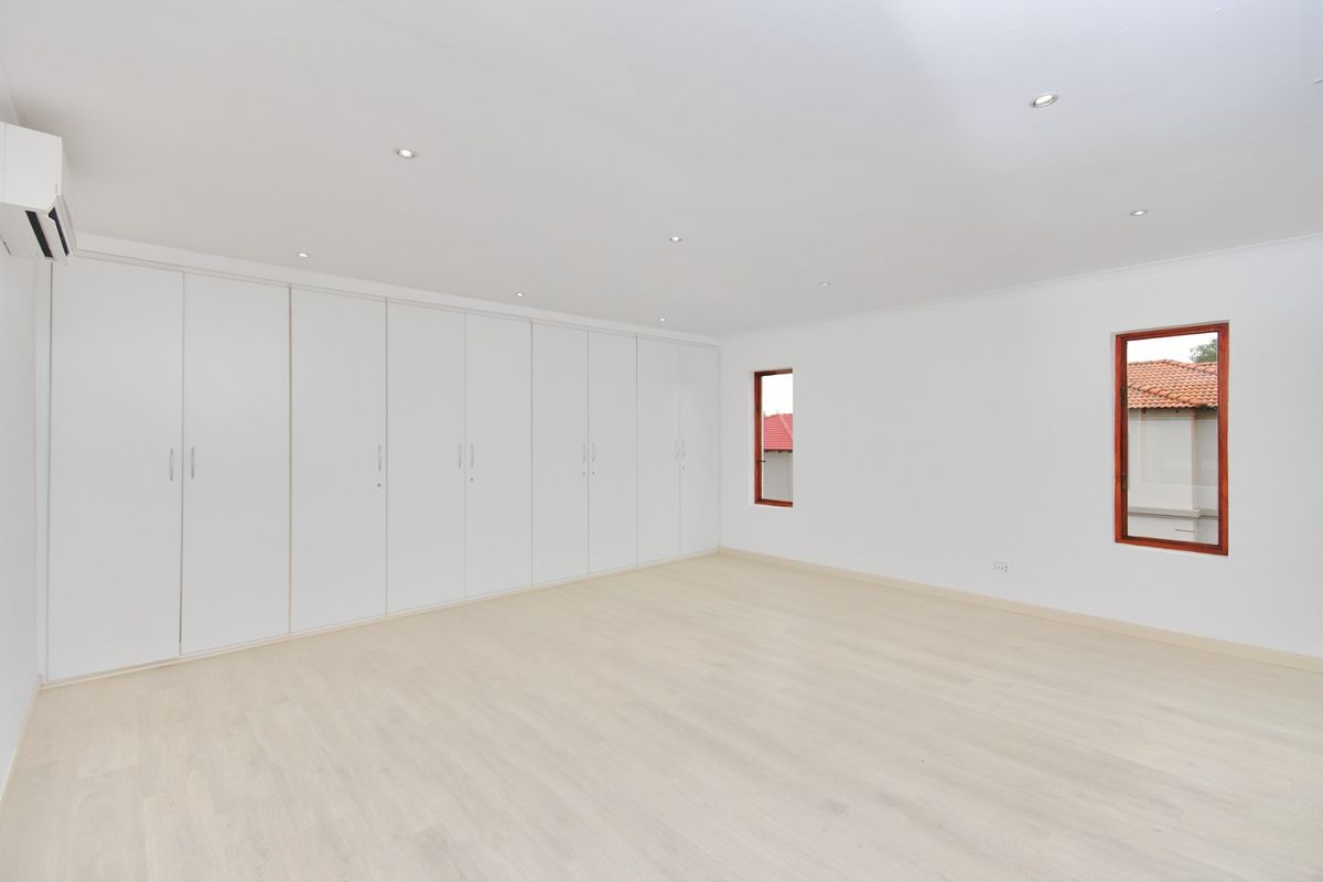 Spacious, bright bedroom featuring extensive built-in cupboards, modern laminate flooring, recessed lighting, and a wall-mounted air conditioning unit.