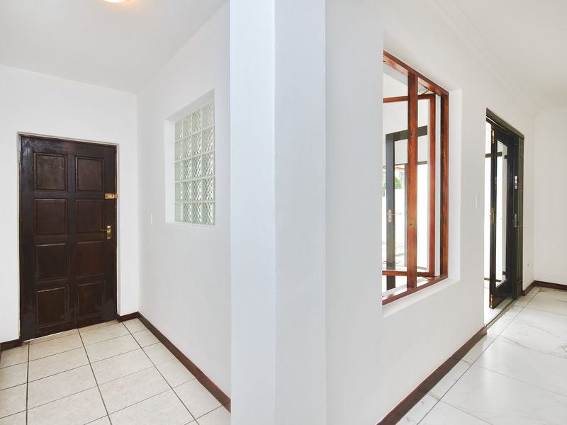 A bright, empty hallway featuring tiled flooring, a decorative glass block window, and timber-framed windows and doors.