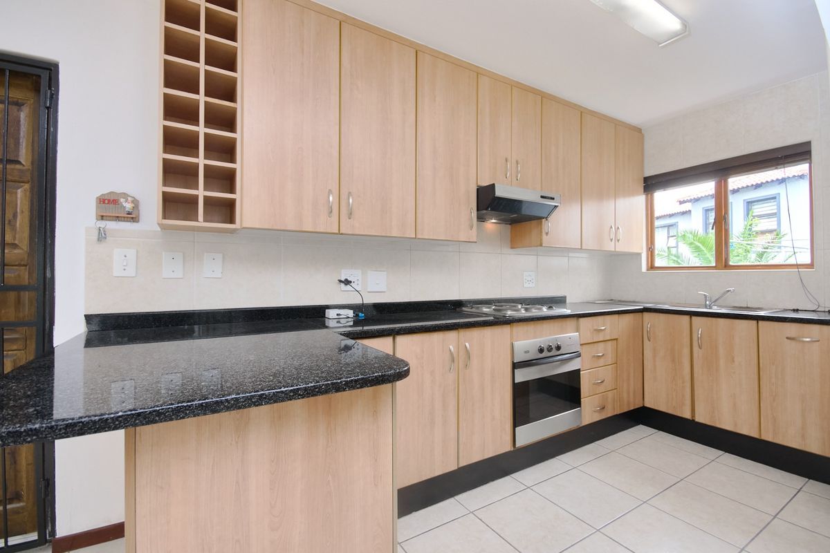 A functional kitchen featuring light wood cabinetry, dark granite countertops, built-in oven, gas hob, and tiled flooring with a neutral backsplash.