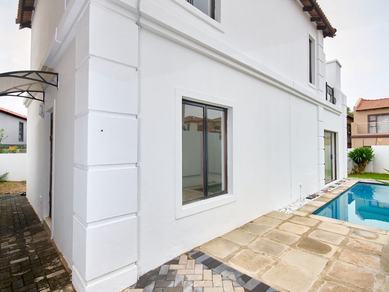 Rear exterior view featuring a swimming pool, paved patio area, and white rendered walls with modern window and door fixtures.