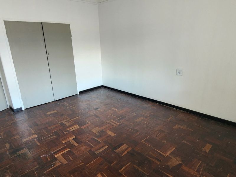 An empty bedroom featuring original parquet flooring and built-in cupboards, presenting a blank canvas for renovation or interior design updates.