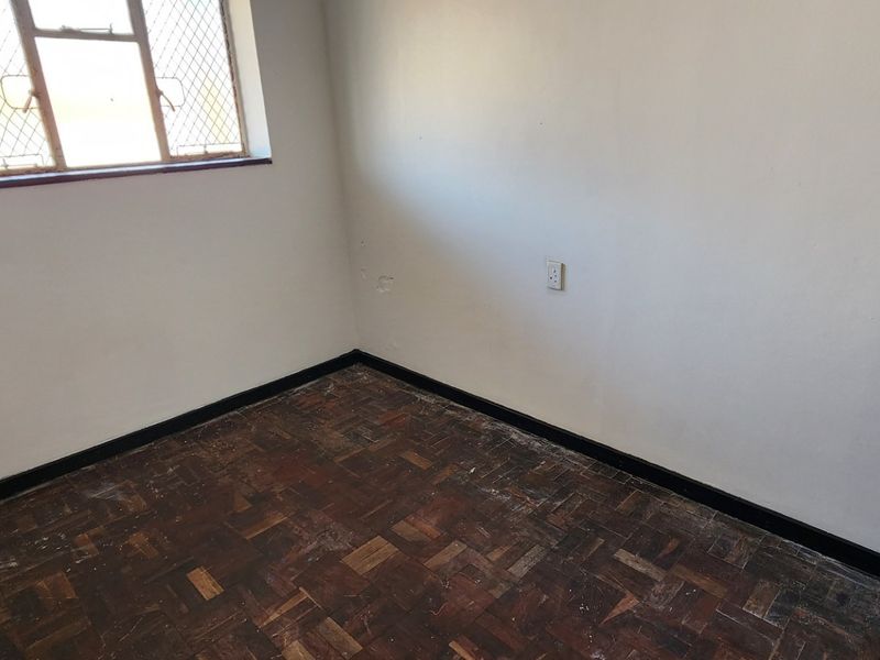 An empty bedroom featuring original parquet flooring, security bars on the window, and neutral wall finishes, ready for renovation or staging.