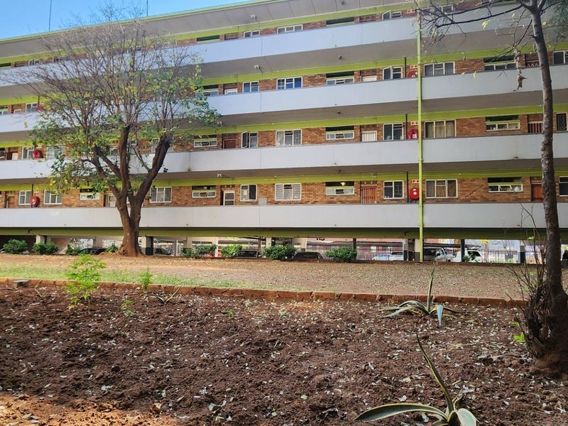 Rear view of a multi-story apartment complex featuring brick facade, open balconies, and ground-level undercover parking facilities.