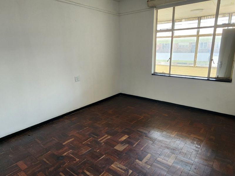 An empty bedroom featuring original parquet flooring and a large window, offering a blank canvas for renovation and interior design updates.