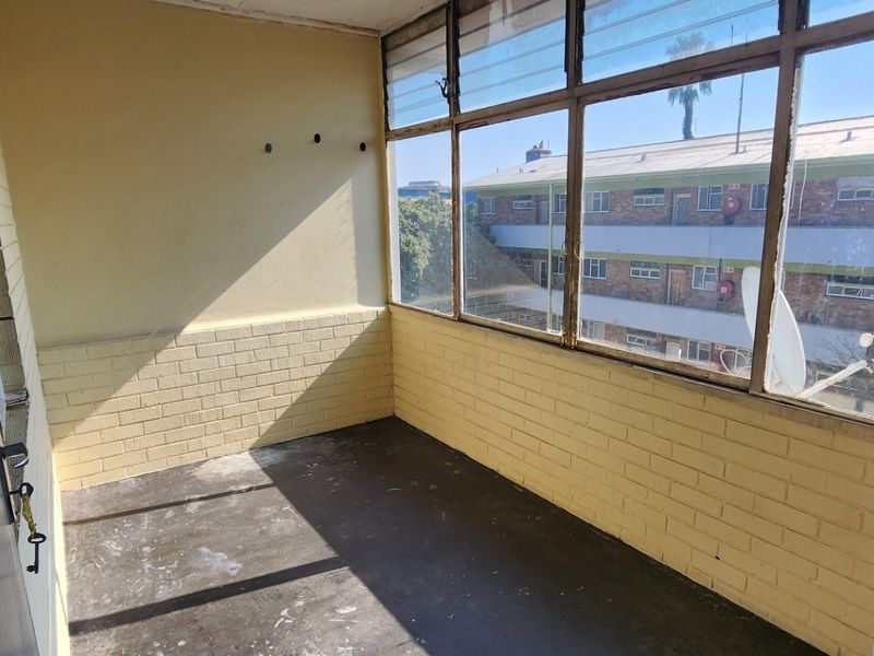 An enclosed balcony featuring brick walls and large windows, offering a view of the surrounding apartment complex.