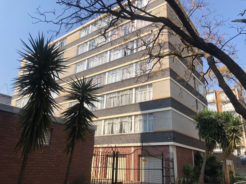 Exterior view of a multi-story apartment building featuring a brick facade, secure gated entrance, and perimeter security fencing.