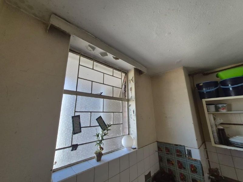 A kitchen area showing significant wear, including peeling paint and damaged window frames, requiring maintenance and cosmetic updates to improve the space.