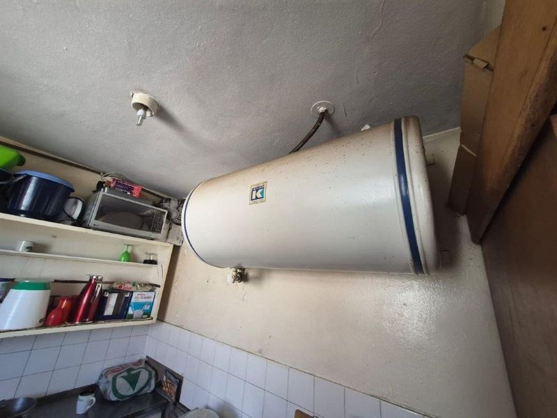 Utility area featuring a wall-mounted electric water heater, tiled splashback, and built-in shelving for storage.
